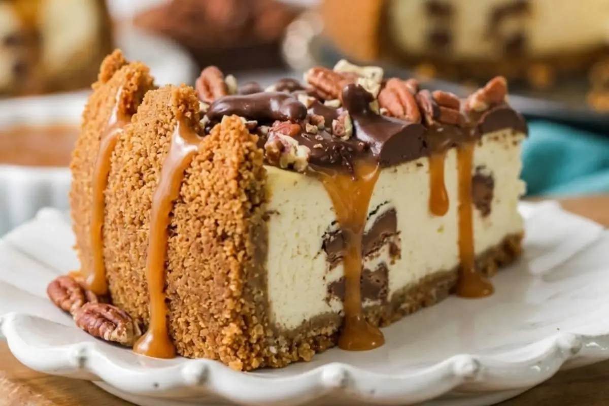 Easy Turtle Cheesecake_ A decadent slice of easy turtle cheesecake on a white rustic ceramic plate, featuring a thick crumb crust, a creamy center studded with chocolate, and topped with a rich layer of chocolate, pecans, and dripping caramel.