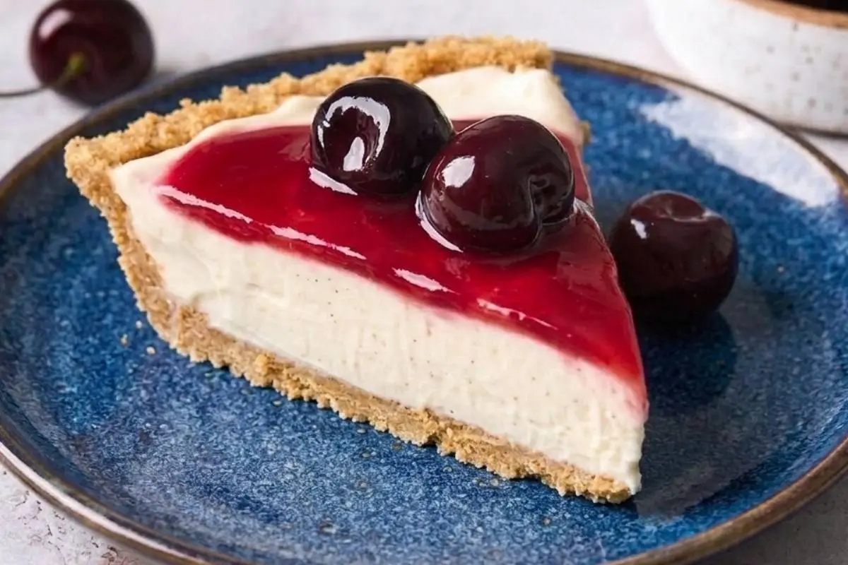 The Best Philadelphia No-Bake Cheesecake Recipe 3 A single slice of Philadelphia no-bake cheesecake on a vibrant blue plate, topped with a glossy cherry glaze and fresh dark cherries, featuring a perfectly golden graham cracker crust.