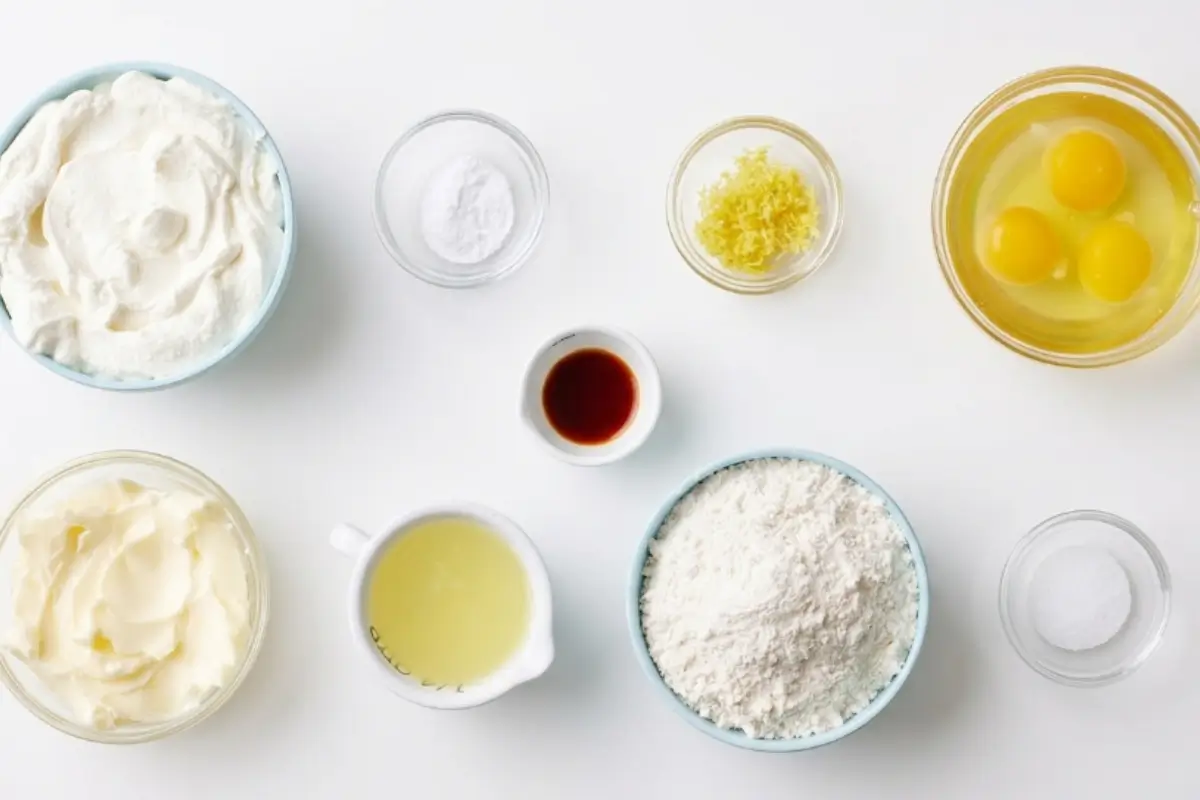 The Key Ingredients For lemon ricotta cake recipe A beautiful overhead view of fresh ingredients, including creamy ricotta, bright lemon zest, farm-fresh eggs, and flour in simple glass and ceramic bowls, ready to be mixed for a classic lemon ricotta cake recipe.