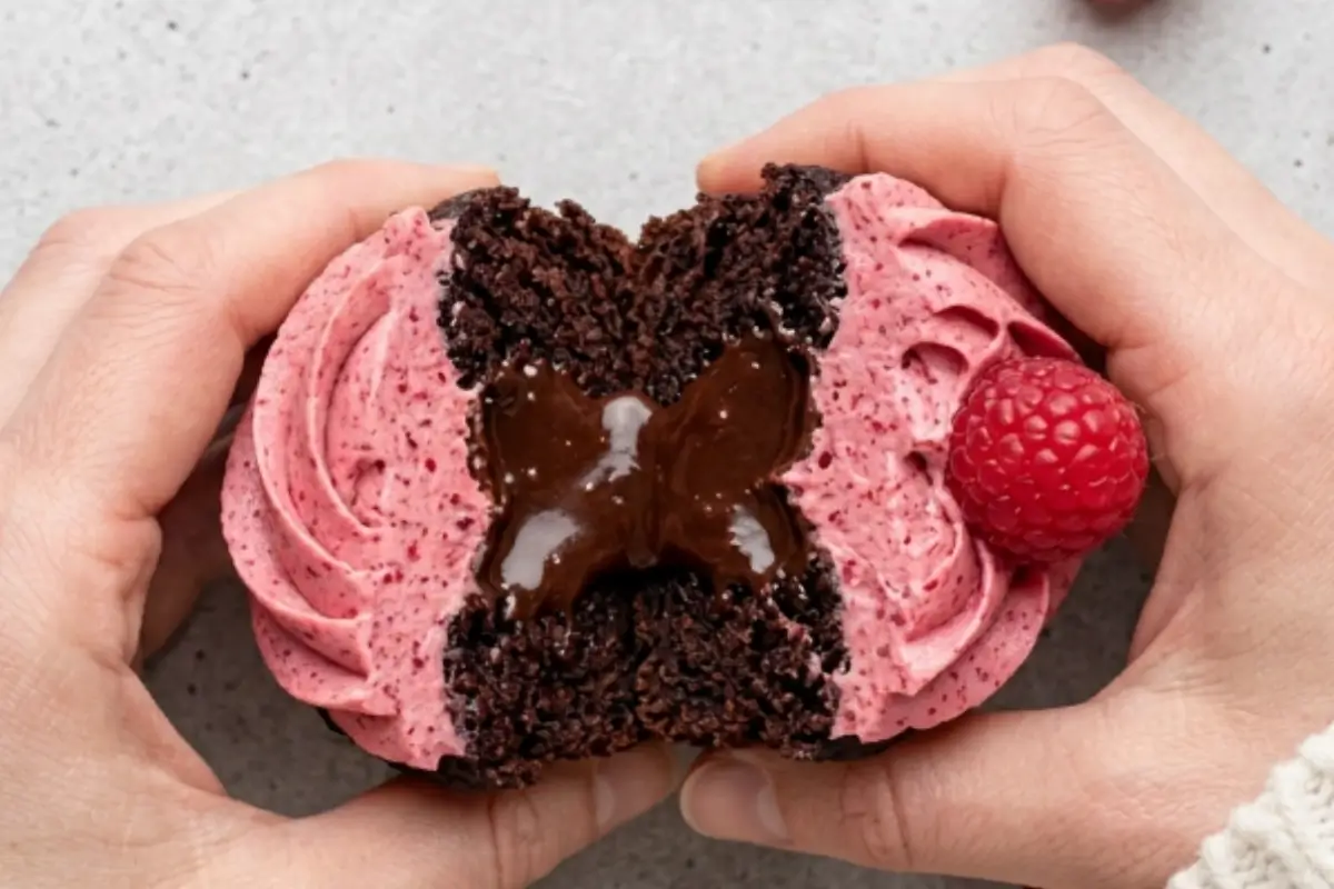 Chocolate Raspberry Cupcakes Recipe Two hands gently pulling apart a freshly baked, decadent dessert to reveal a gooey molten chocolate center, showcasing our favorite chocolate raspberry cupcakes recipe topped with pink buttercream and a fresh berry.