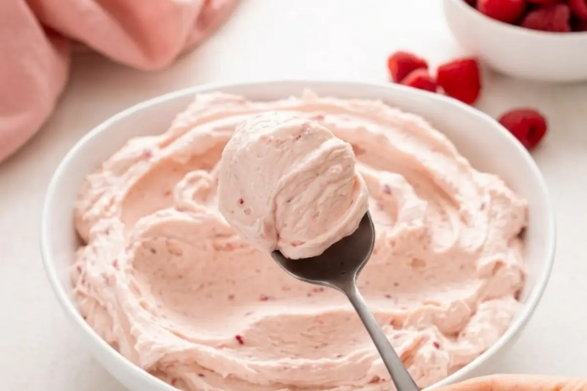 Homemade Buttercream Frosting Ready in 10 Minutes 2 A spoonful of fluffy, pale pink homemade buttercream with real raspberry flecks lifted from a white ceramic bowl.