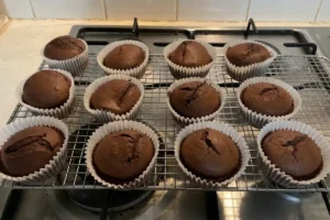 A batch of freshly baked chocolate cupcakes in white liners cooling on a wire rack[cite: 1], demonstrating how to prevent cupcake wrappers from peeling.