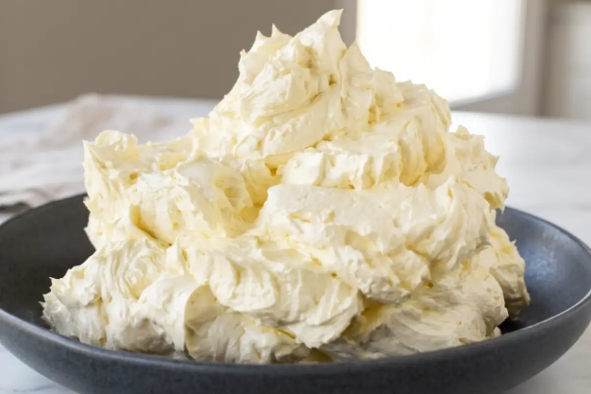 Italian Meringue Buttercream A generous mound of fluffy, velvety Italian meringue buttercream with soft textured peaks resting in a dark ceramic bowl.