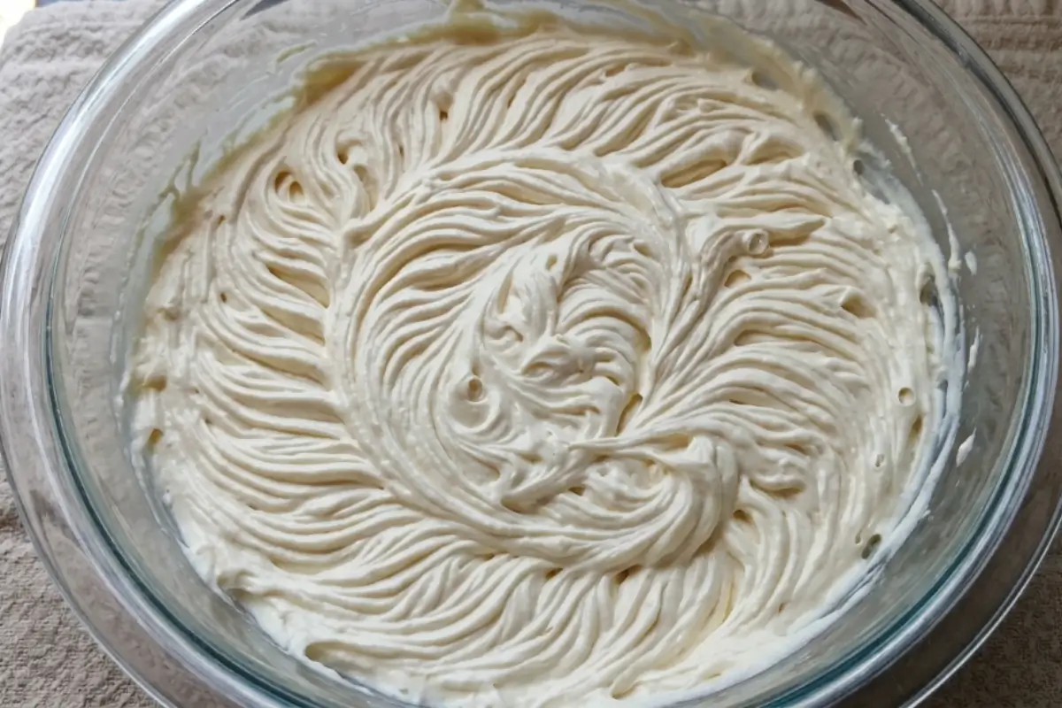 Mascarpone Frosting A large clear glass mixing bowl filled with freshly whipped, creamy mascarpone frosting swirled in rich decorative ridges.