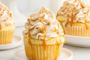 Salted Caramel Filled Cupcakes 14 A close-up view of Salted Caramel Filled Cupcakes topped with a generous swirl of frosting, a drizzle of caramel sauce, and a sprinkle of flaky sea salt on a small white plate